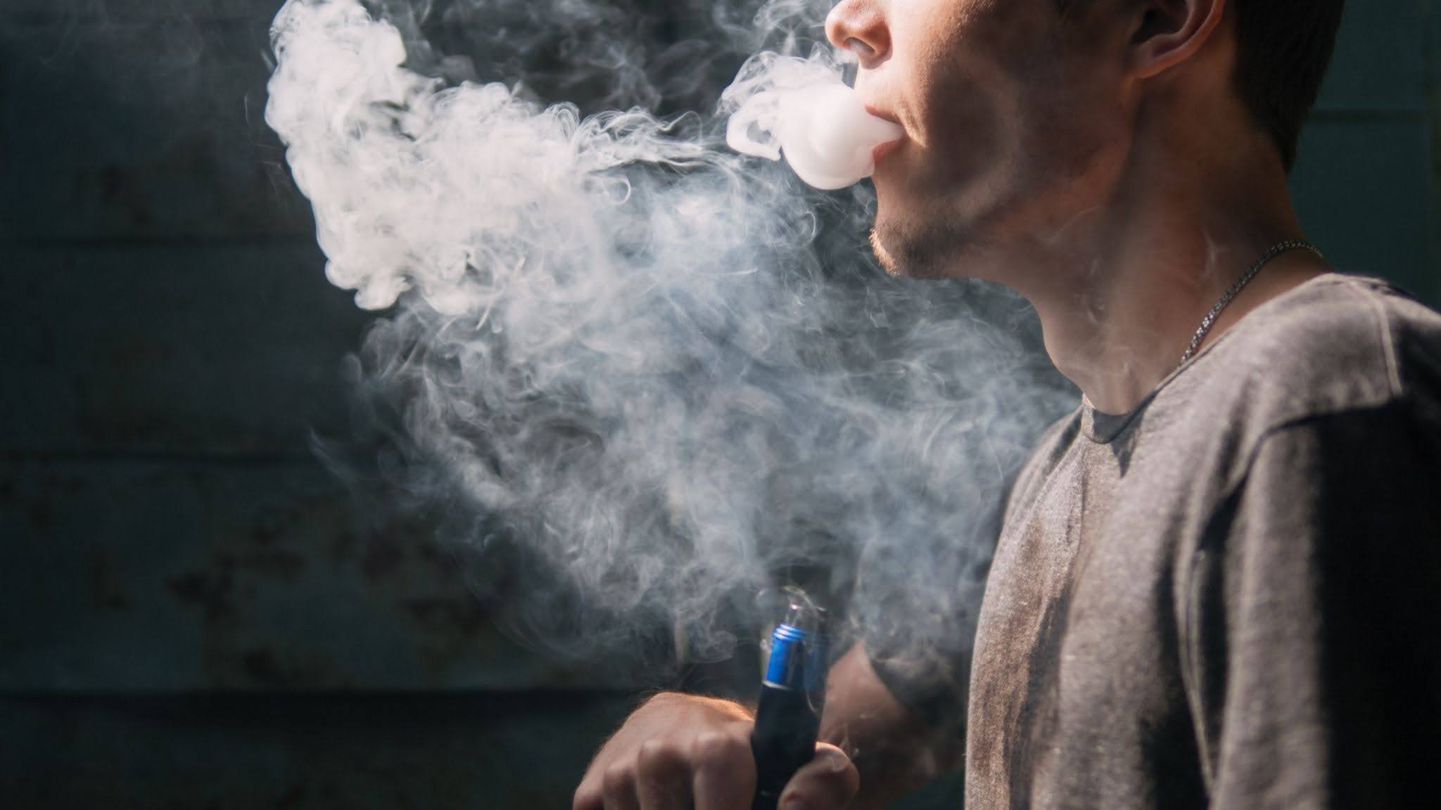 A person using a vape pen, producing clouds of vapor.